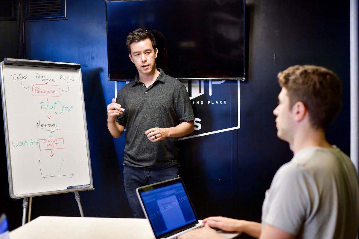 Two men having a meeting with a whiteboard and laptop.