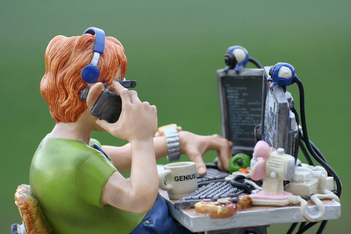 Sculpted programmer making a phone call sitting in front of two screens