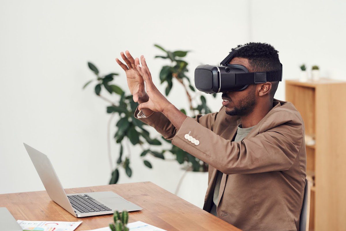  A man sitting at a desk with a laptop and using VR goggles. Online Unity Courses