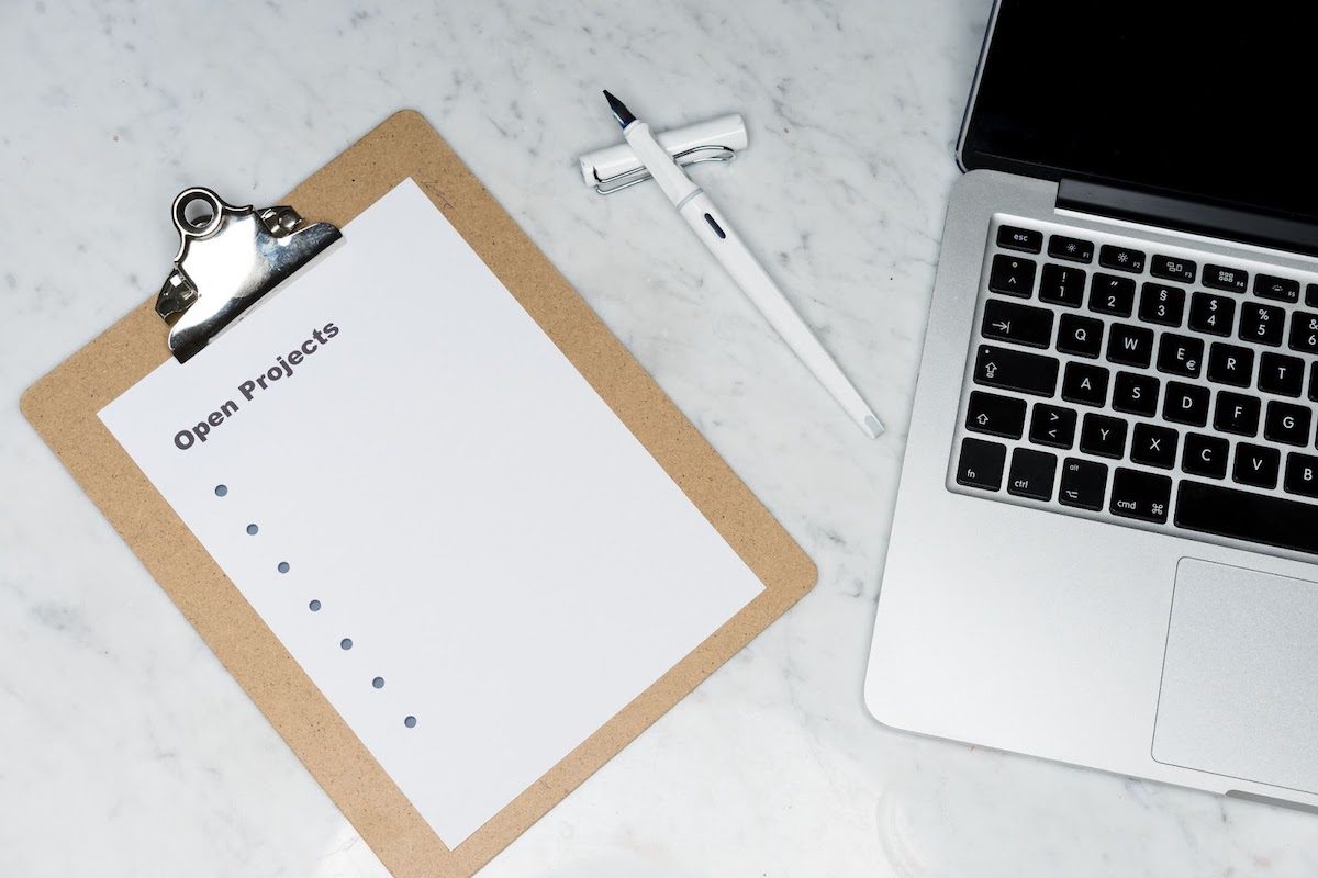 A clipboard with a paper listing open projects next to an open laptop.