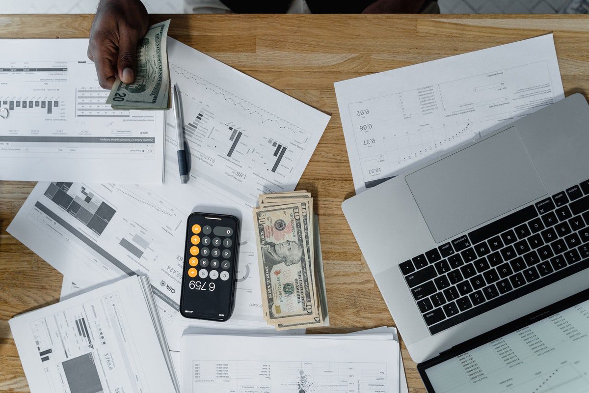 A table with a laptop, papers, phone, pen, and cash and a hand holding out more cash. Financially Rewarding Careers