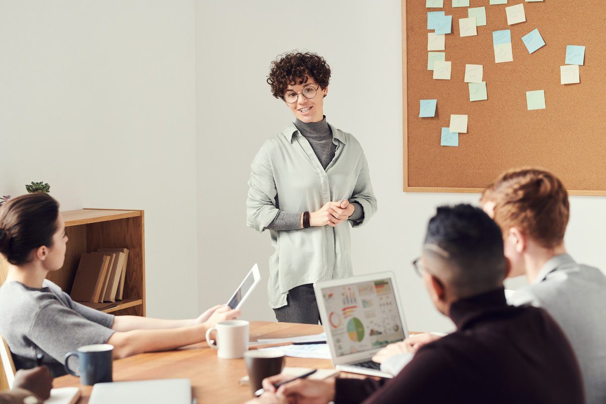 A woman standing in front of a whiteboard, leading a work meeting of seated team members. Philanthropic Careers