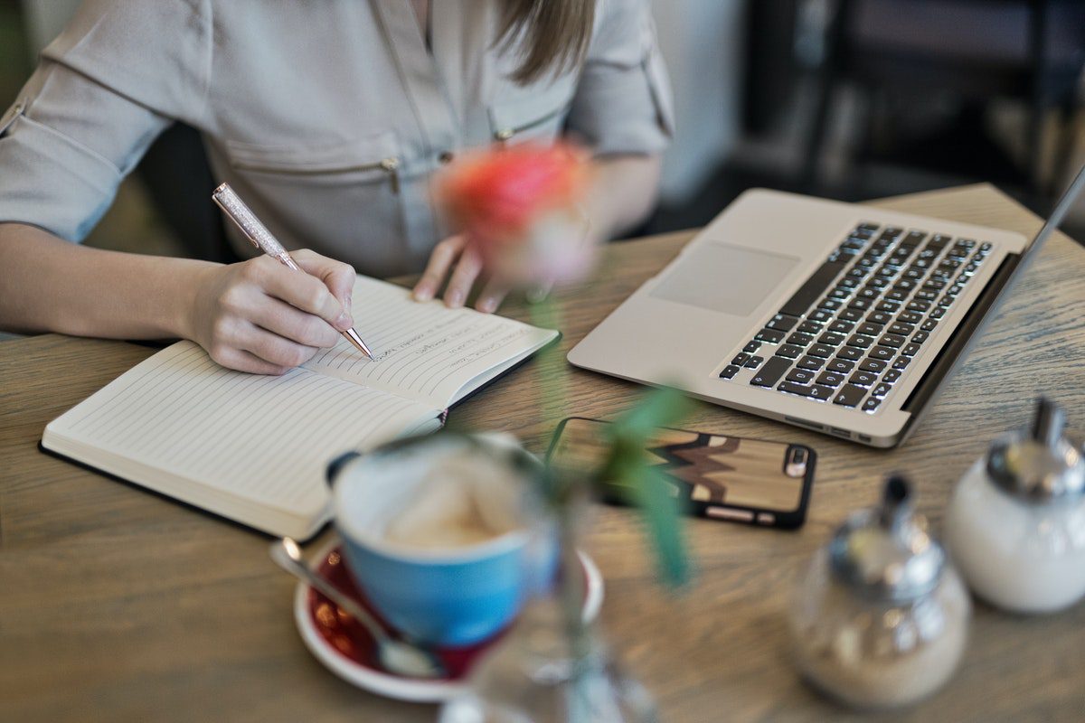 A person writing on a notebook on a white table next to a laptop. Account Executive Cover Letter