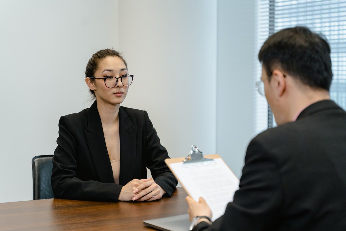A woman sitting across a desk from a prospective employer holding a clipboard. Entry Level Cover Letter