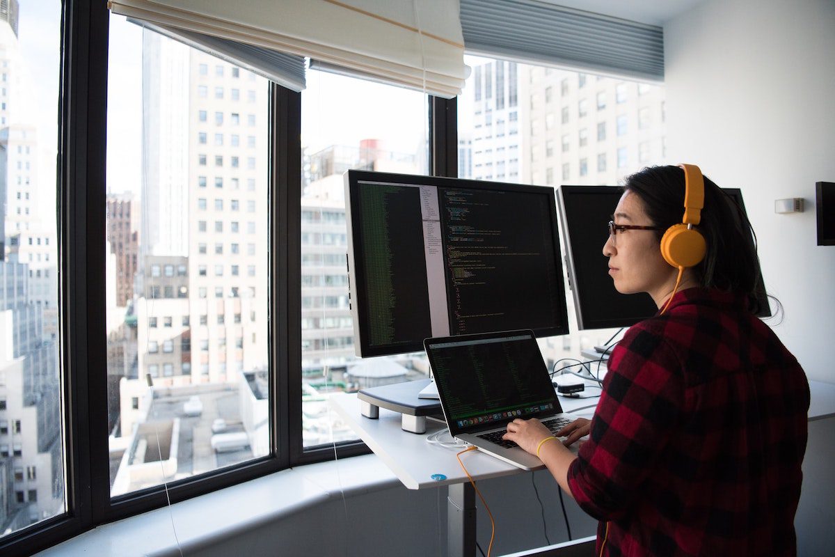 A woman wearing a headset writing code on a laptop. Full Stack Developer Job Satisfaction