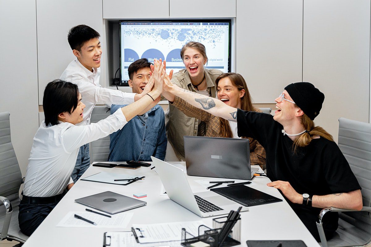 A group of professional developers reach out for a high-five while collaborating. Mobile Developer Job Satisfaction
