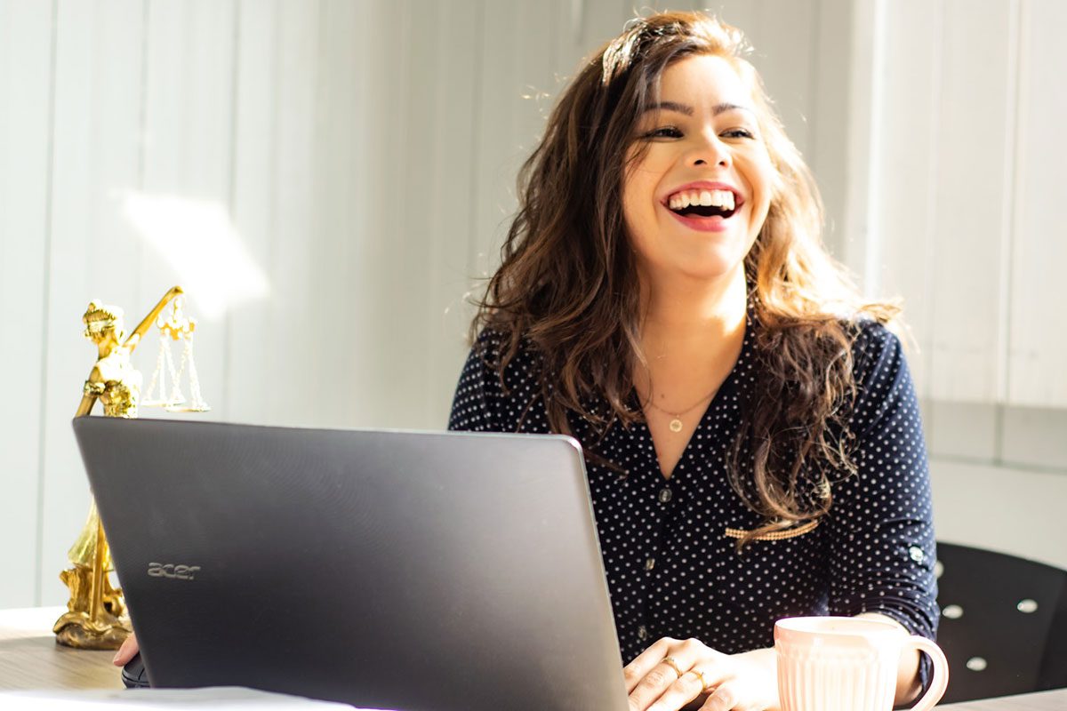A female executive laughing and working on her laptop. Program Manager Cover Letter