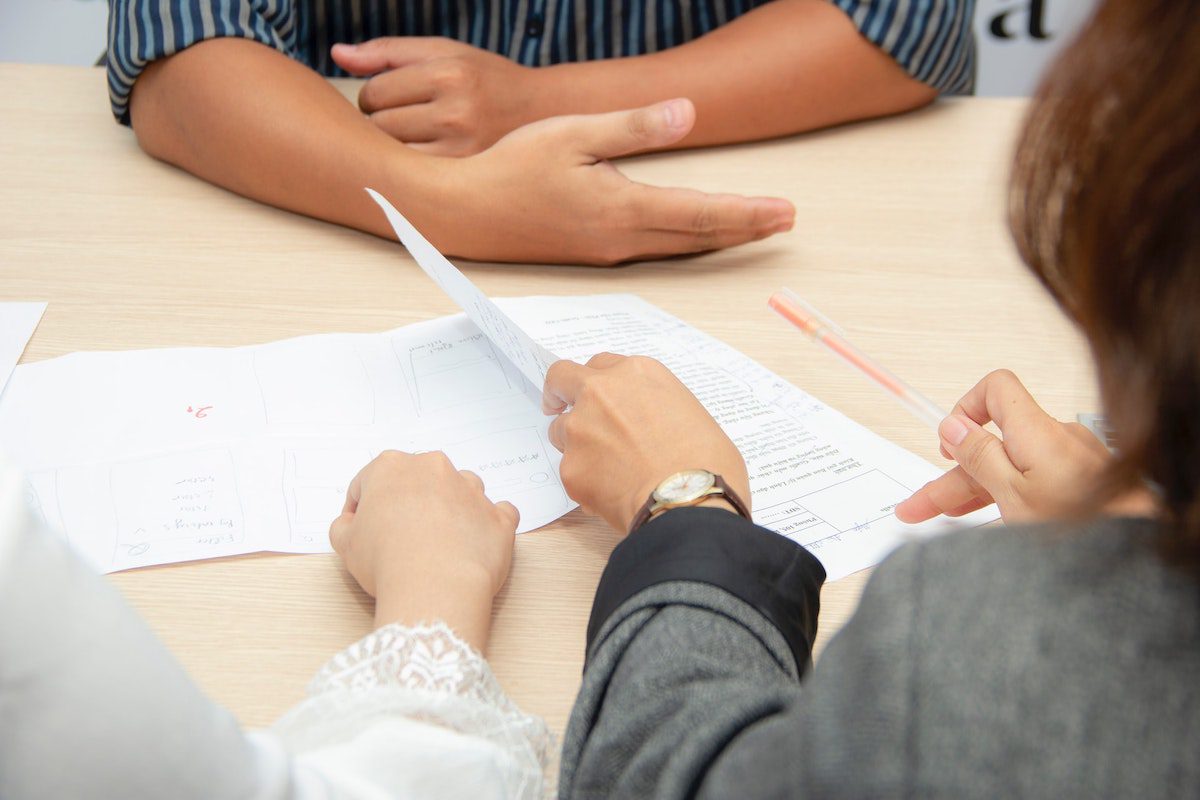 Three people holding sheets of paper on a table. Research Analyst Cover Letter