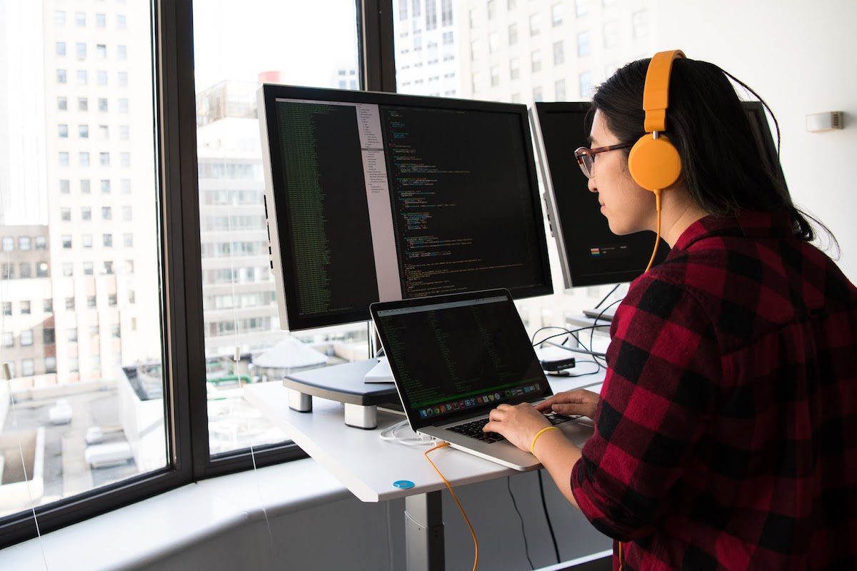 A woman typing on a laptop and programming on multiple computer screens at once.