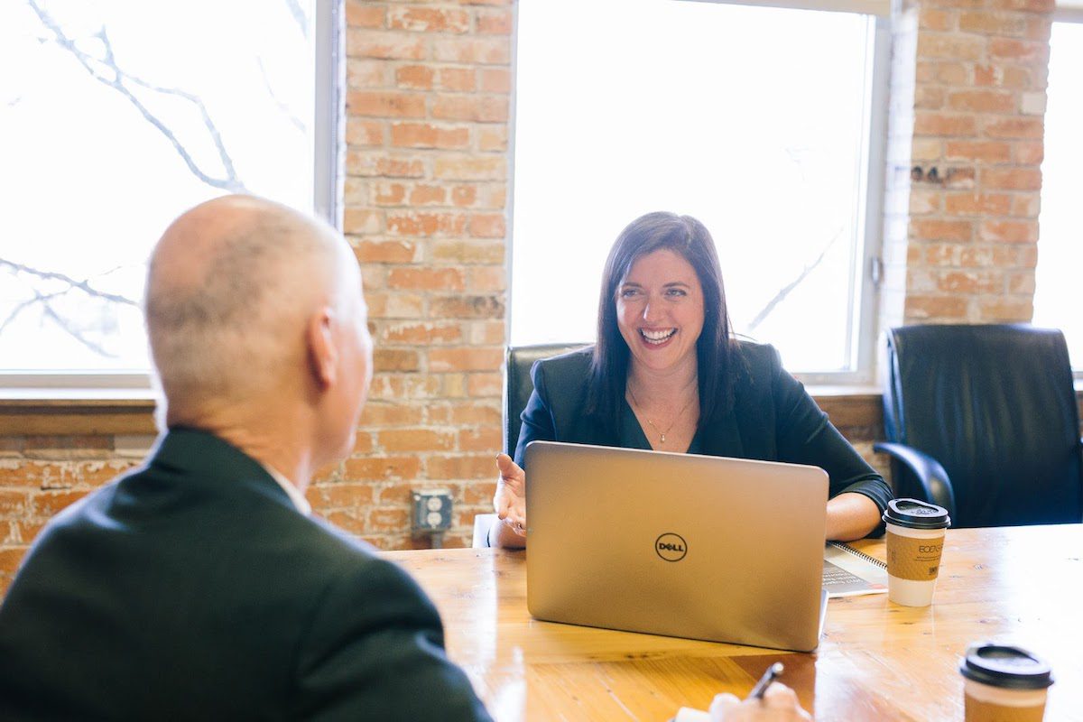 A woman using a laptop in a meeting with a man and a brick wall background.