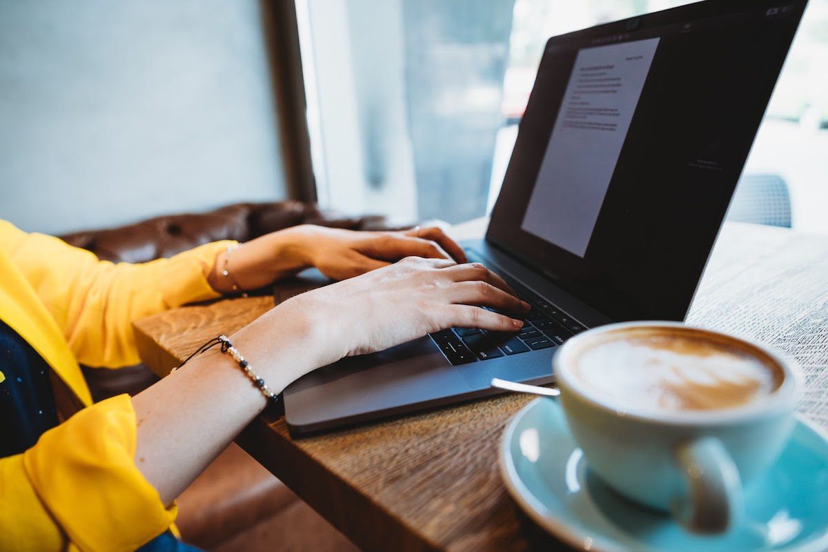 Two hands typing an Upwork profile on a laptop keyboard, with a cup of coffee sitting close by.
