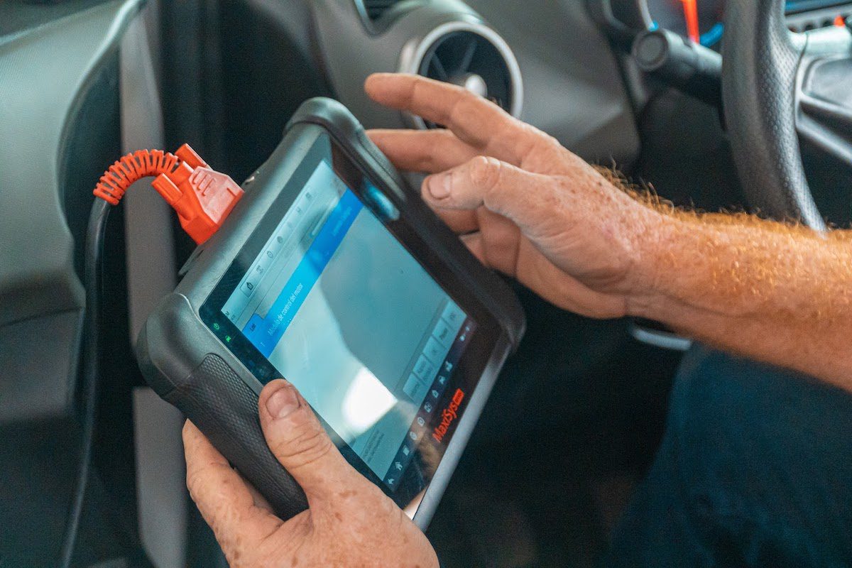 A man holding a diagnostic device connected to a car’s electronics.