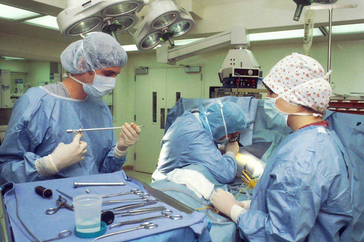 Nurses holding medical equipment and helping a surgeon in the operating room.