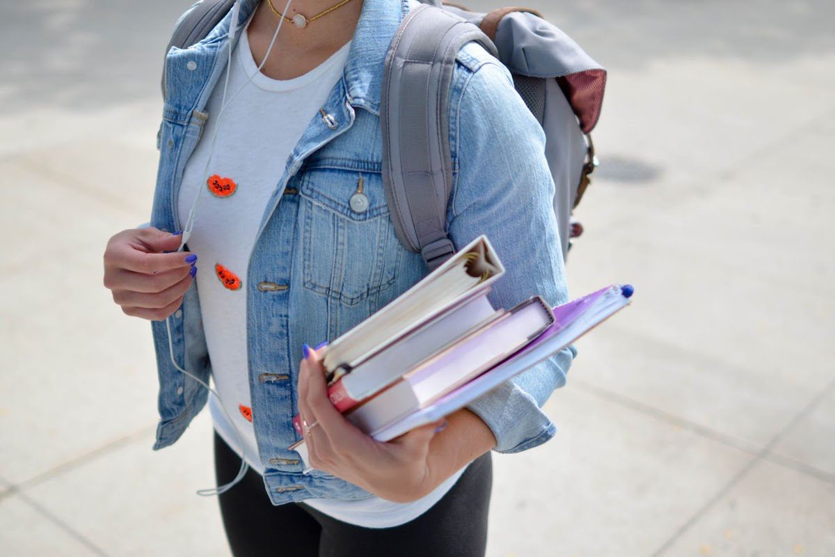 Woman in jean jacket wearing headphones and holding books