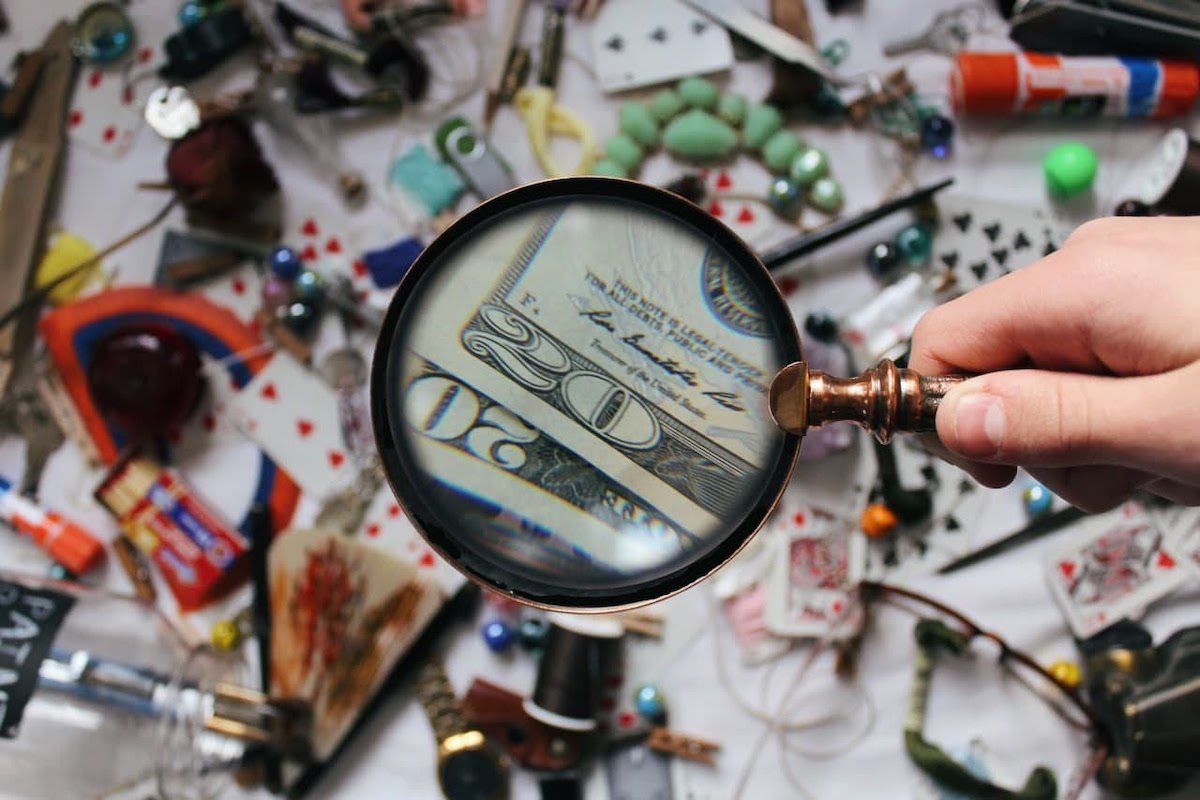 A hand with a magnifying glass finding extra income among randomly scattered items.