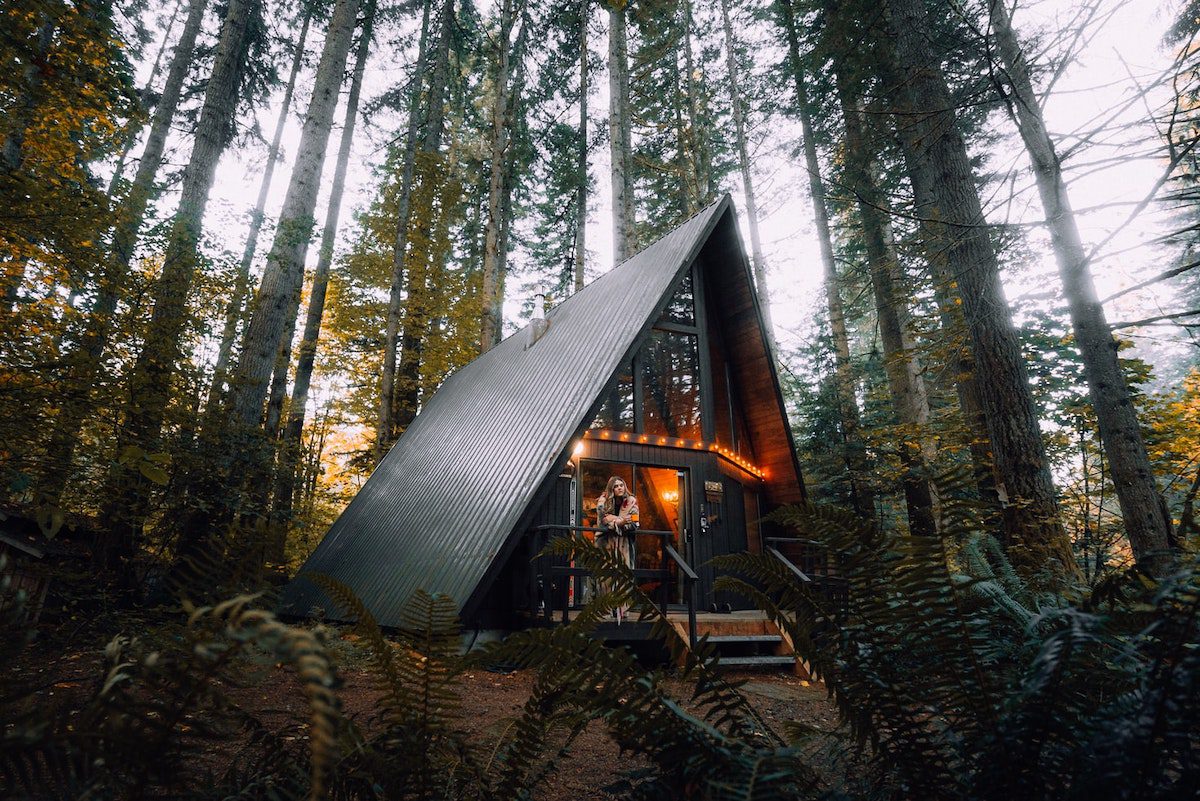 Person standing on the deck of a modern Airbnb cabin in the woods  How Much Can You Make on Airbnb?