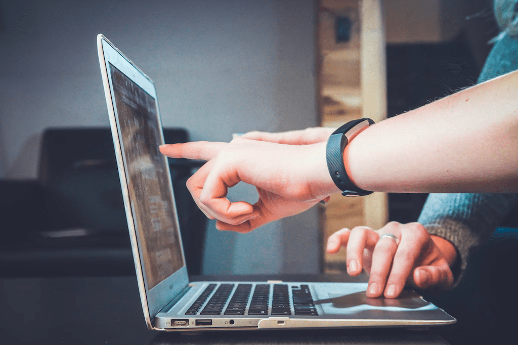 Close-up photo of the hands of two product development professionals working on a laptop. One hand is using the trackpad and one hand is gesturing at the screen.