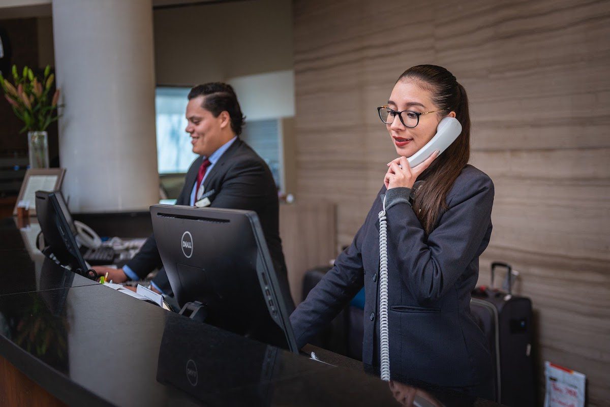 A couple of hourly workers standing behind a hotel desk and working. Jobs That Pay $13 an Hour