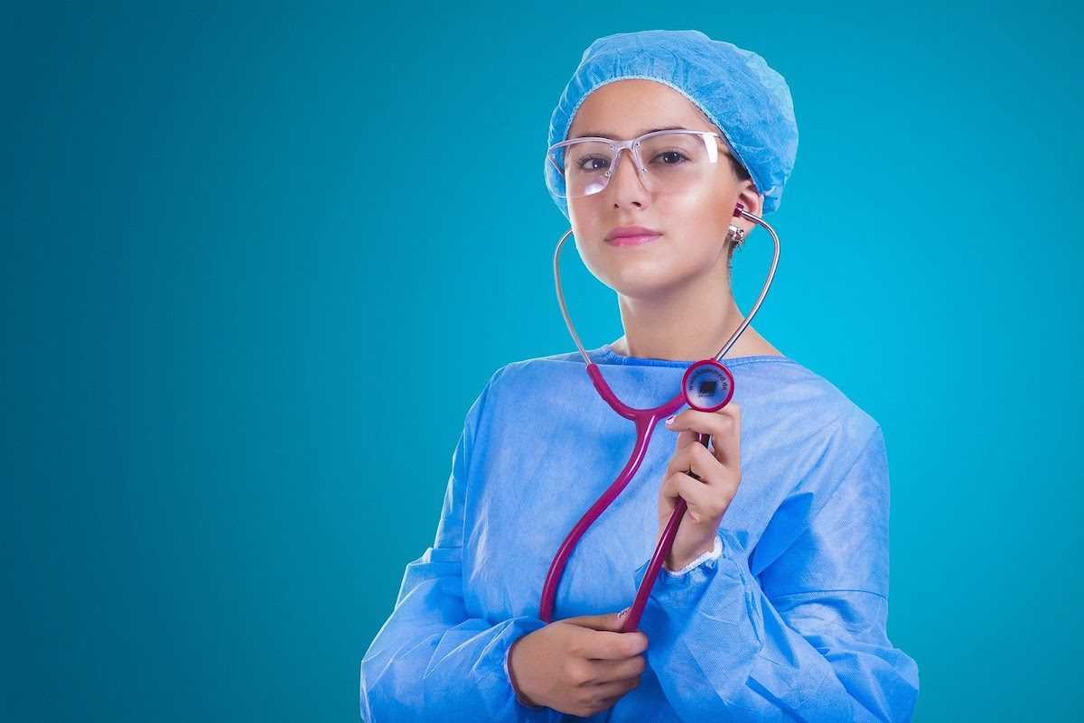 A woman in blue personal protective equipment and glasses holding a pink stethoscope. The Best Healthcare Companies in 2022