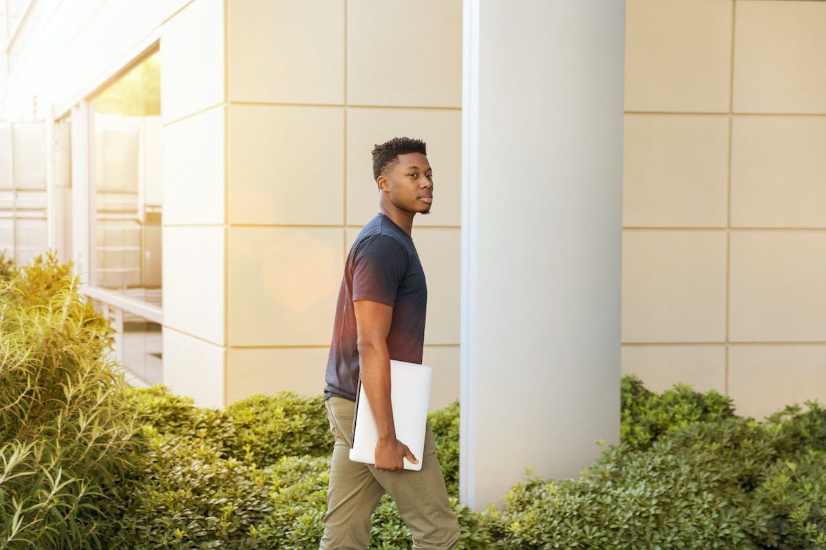 A man holding a laptop while walking next to a building