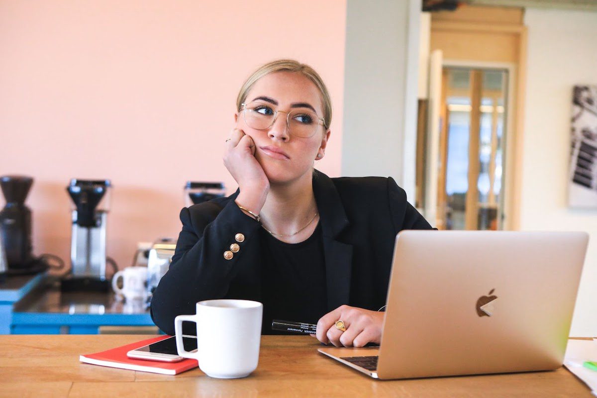 A woman dressed in black in front of a computer and a cup of coffee