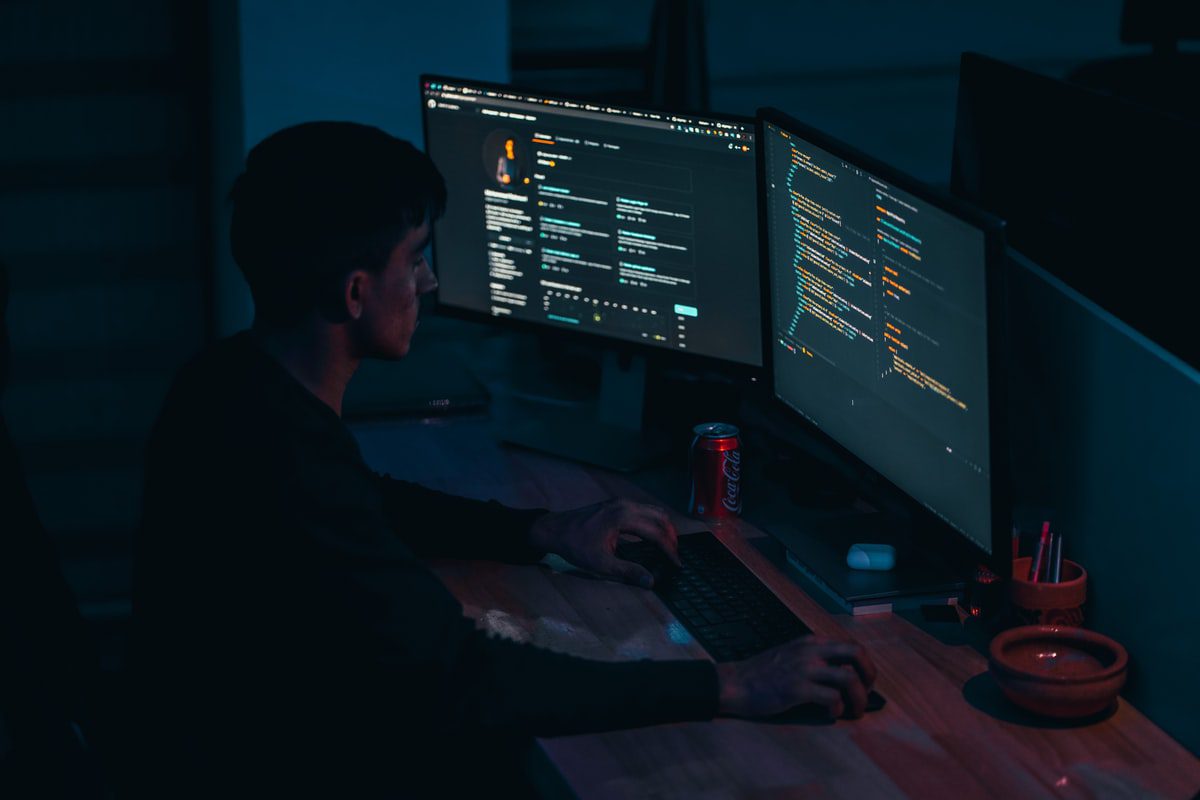 A man writing lines of code into a standalone source code editor tool on his dual desktop monitors.