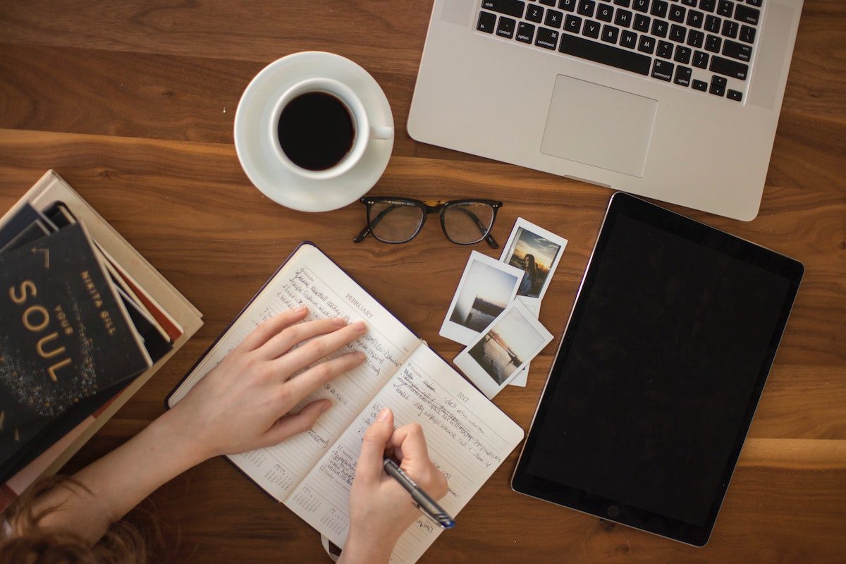 A person writing with a pen in front of a tablet and a laptop. Advertising Portfolio