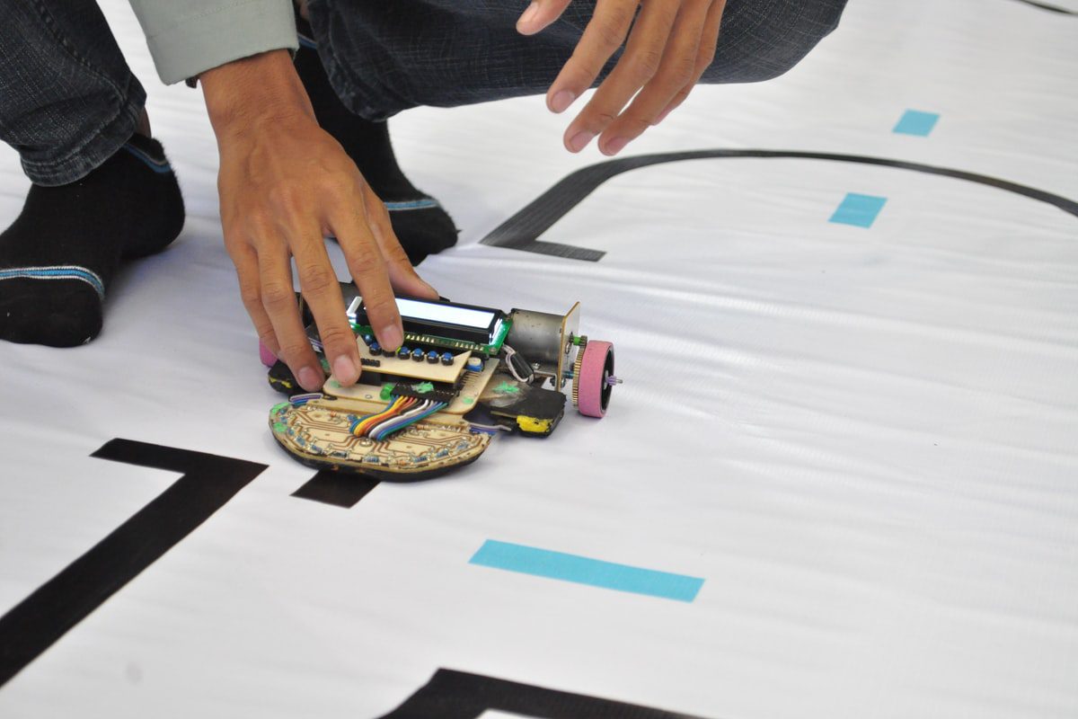 a person holding a simple robot car on a white plastic mat