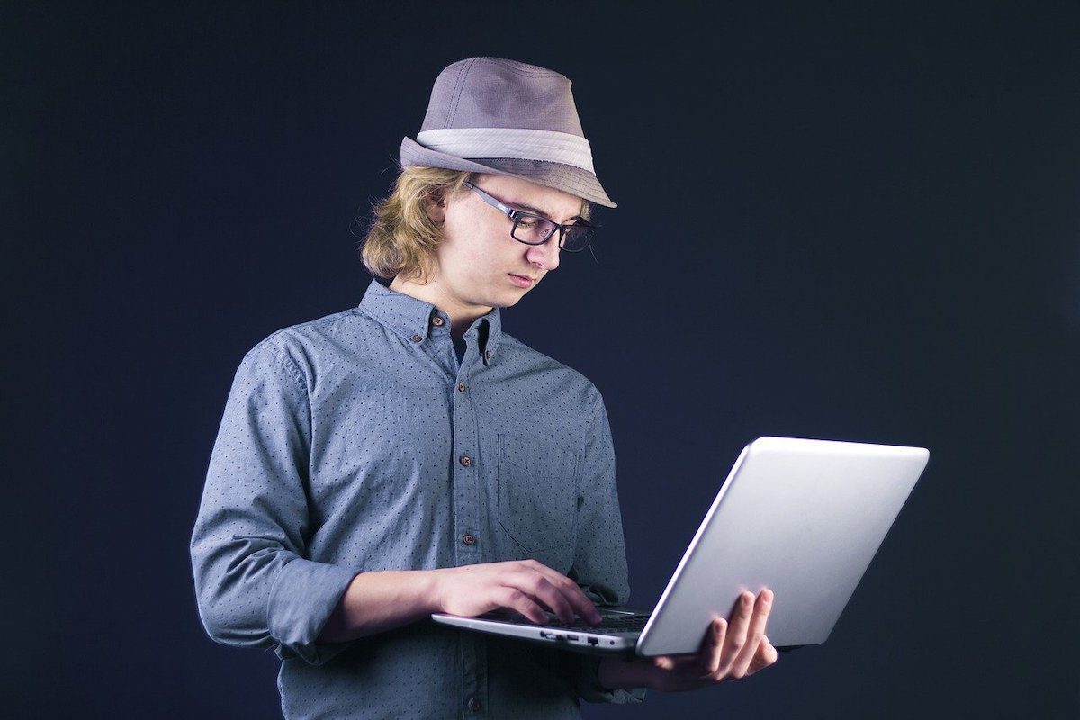 a man standing and holding an open laptop while typing. Computer Science Portfolio