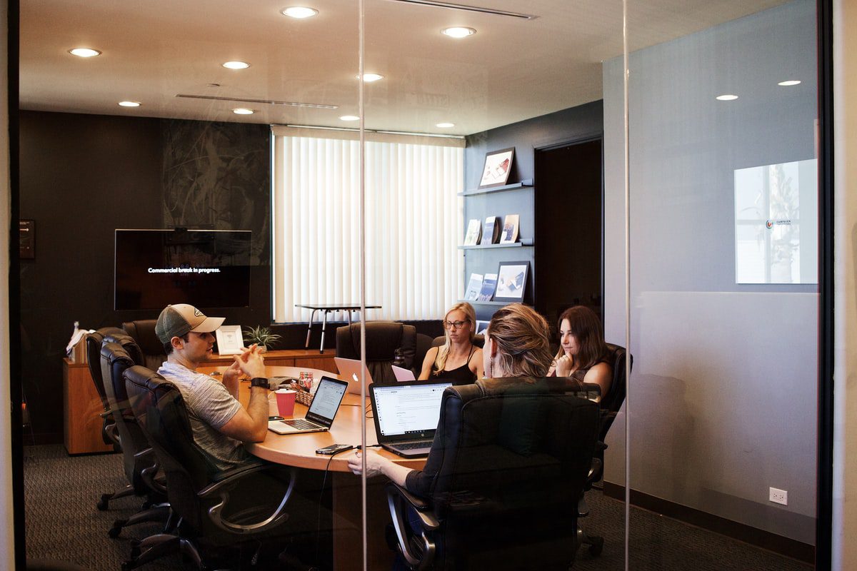 four people in an office at a desk with laptops
