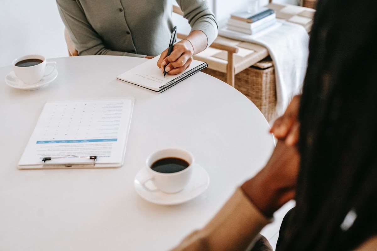 An interviewer writing on a notepad sitting across from a potential employee.