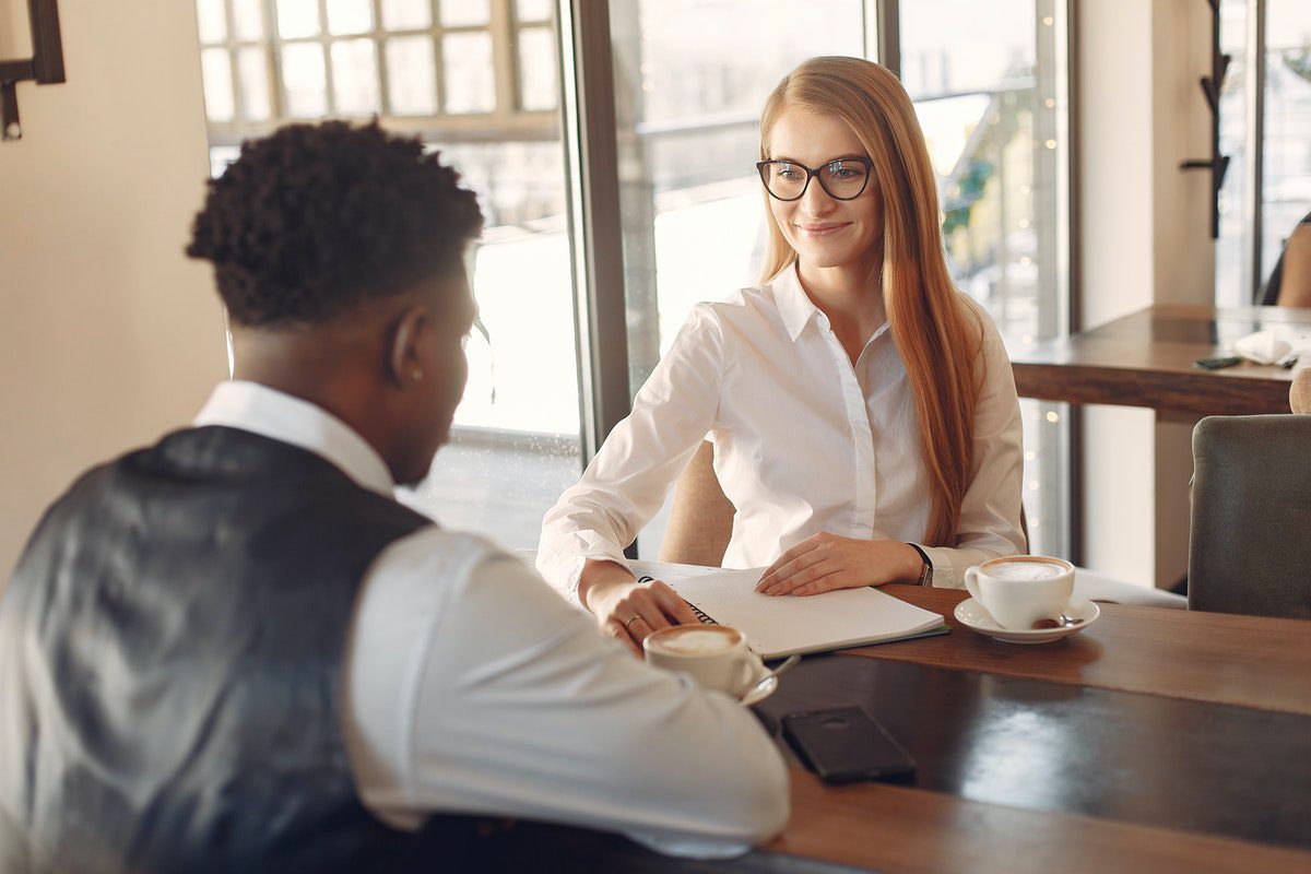 woman interviewing a man across a desk with two coffees. Ironhack Interview Questions