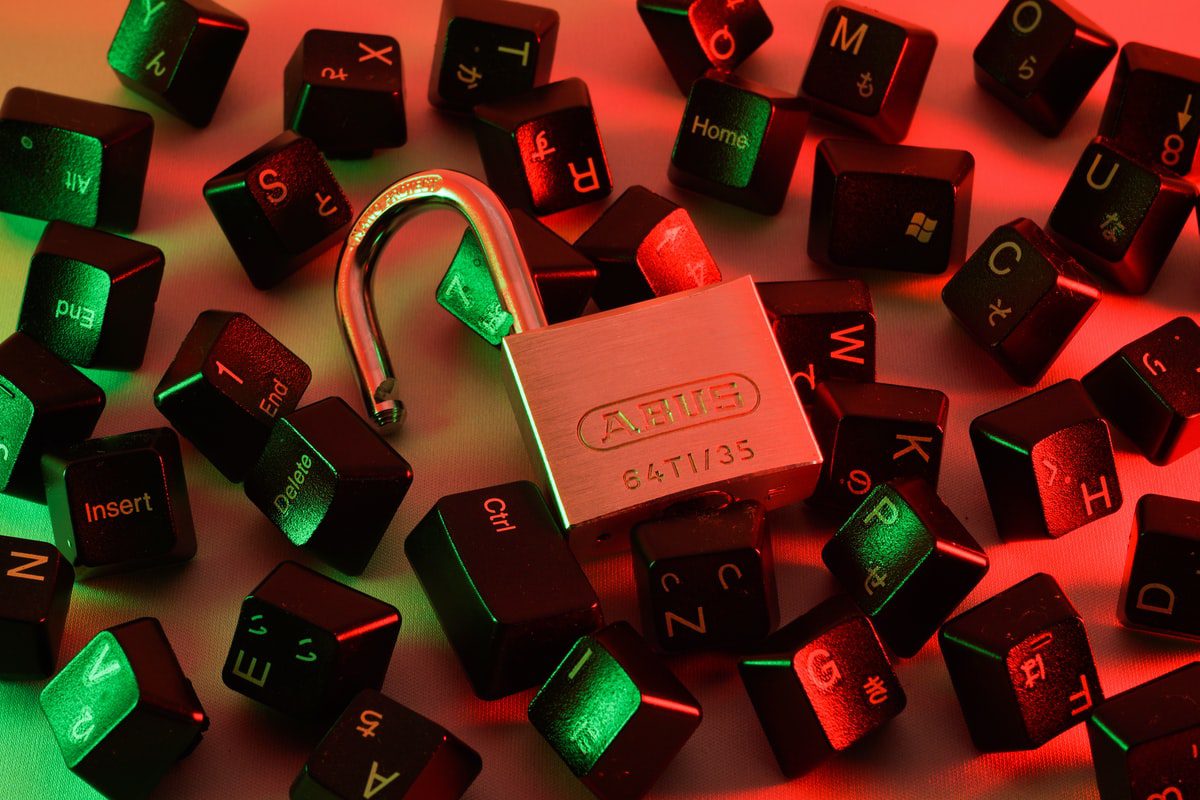 A picture of an open padlock placed on several computer keyboard keys with a background of red and black lighting. 
