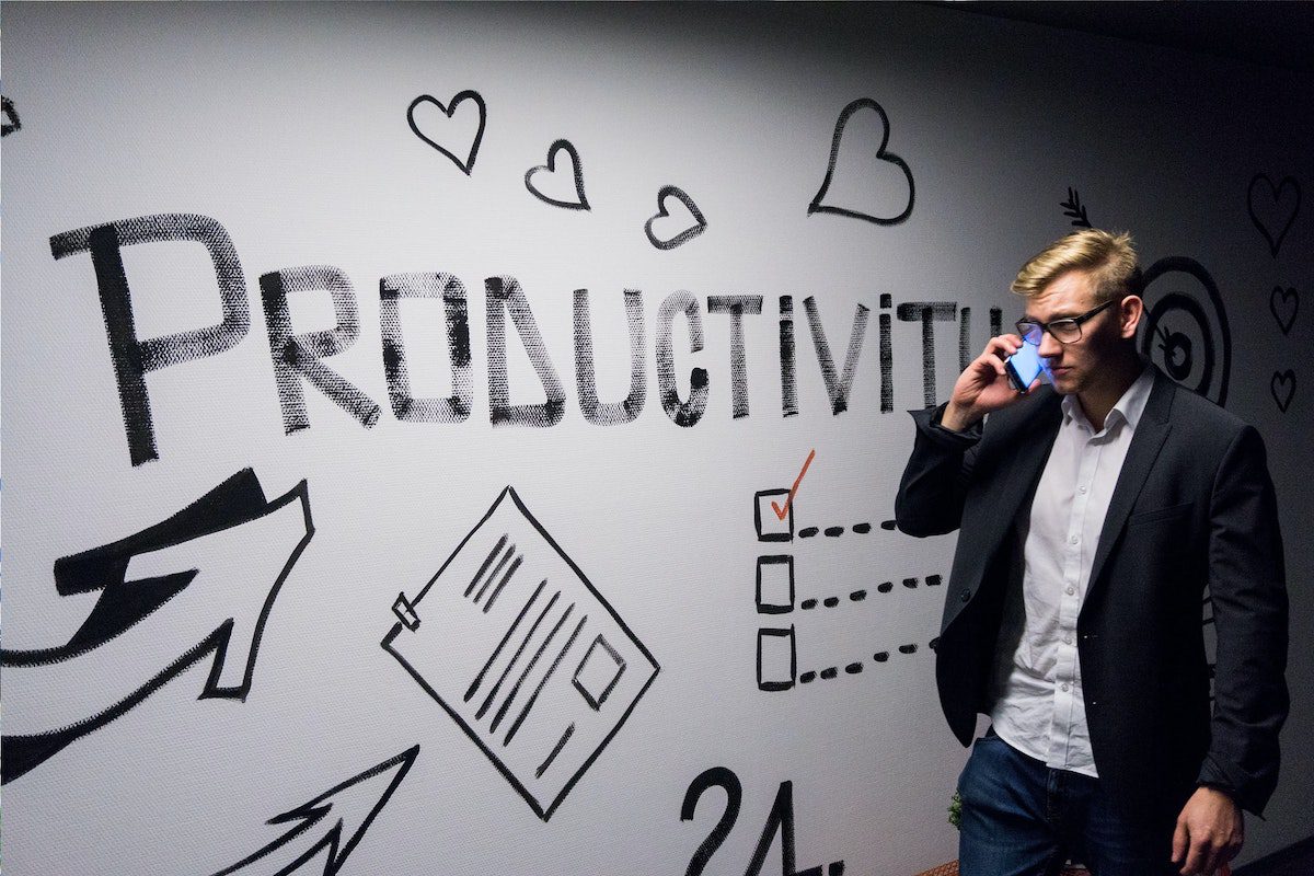 A man in corporate attire answering a call while looking at a productivity board. Project Manager Tools