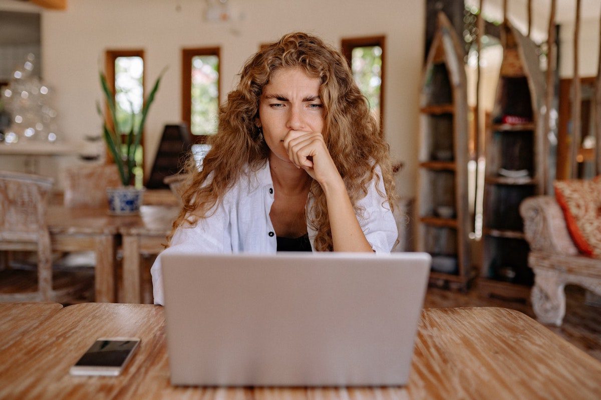 A graphic designer has a pensive facial expression while using a laptop