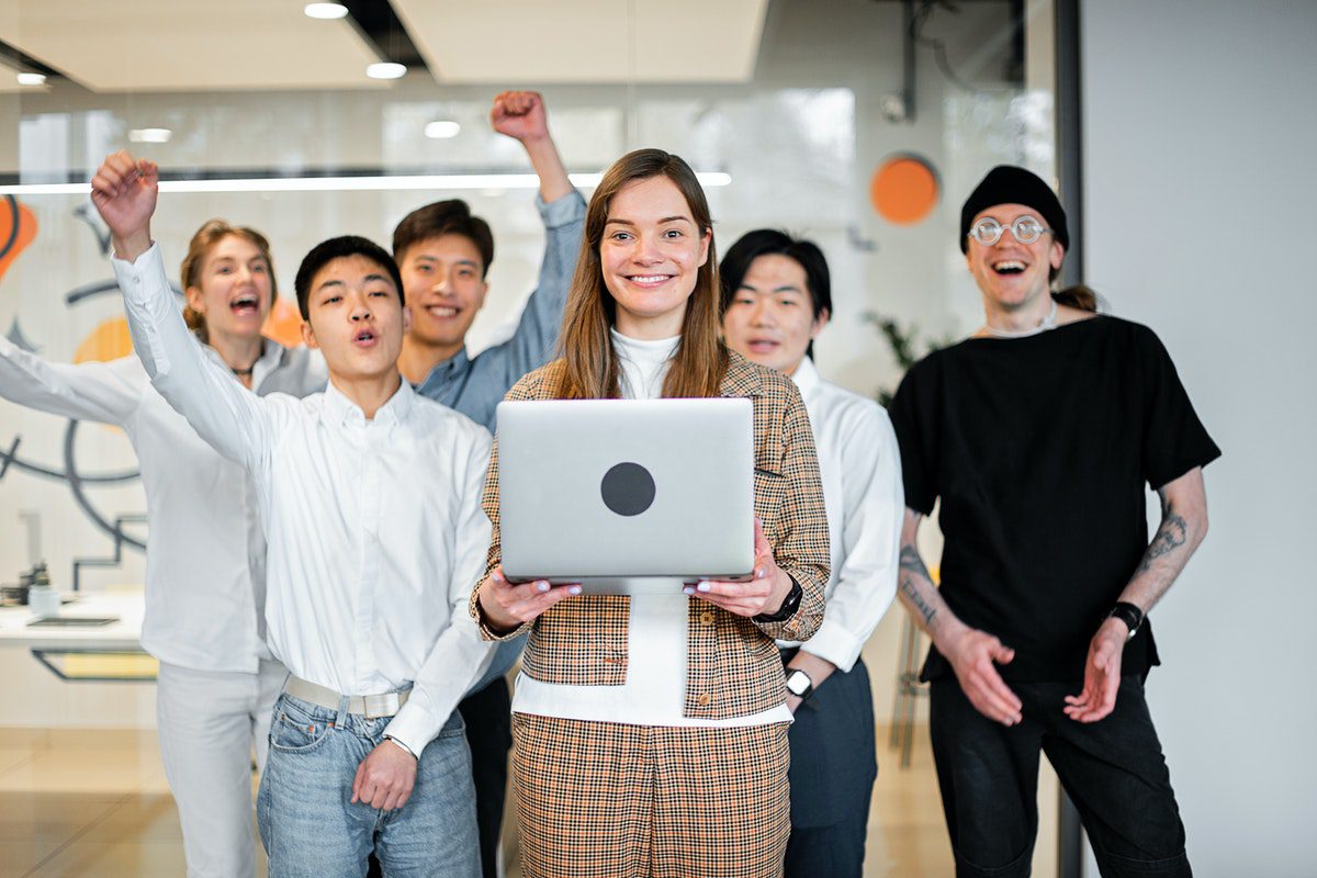 A woman holding a laptop in front of a group of employees. 