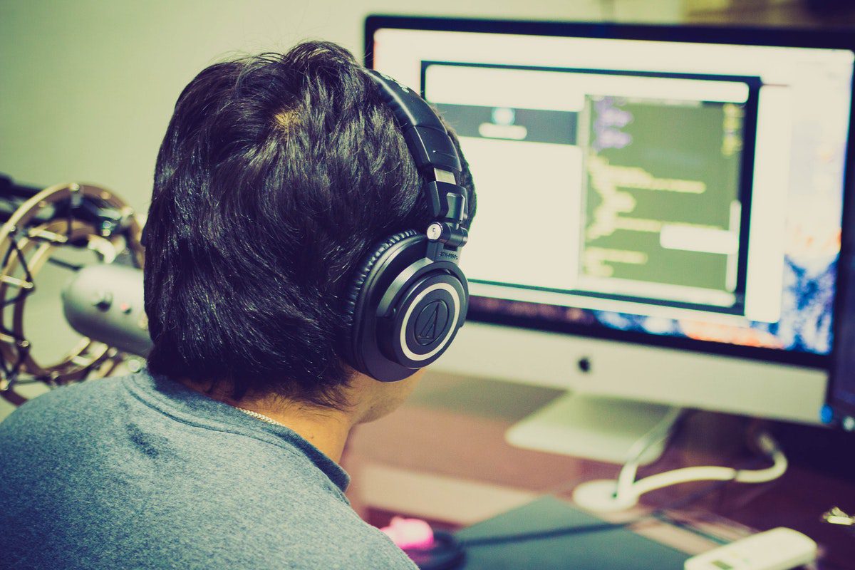 A man with a headset working on a coding project with two computers.