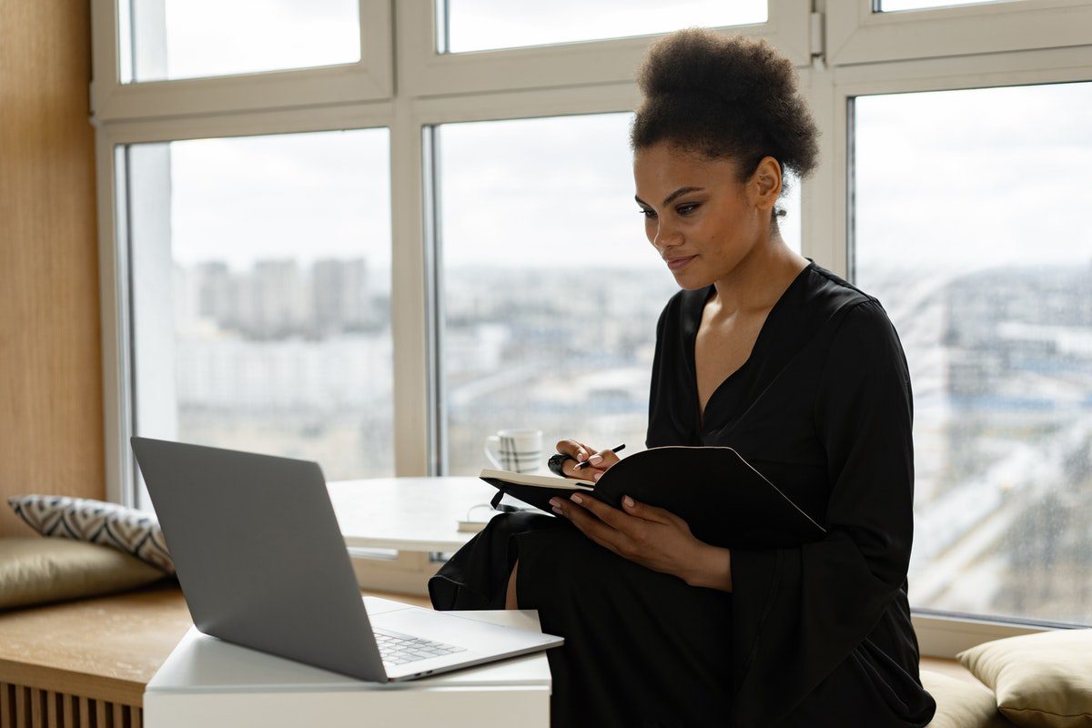 A woman standing in front of a laptop holding a pen and a notebook. Is Excel Hard to Learn?