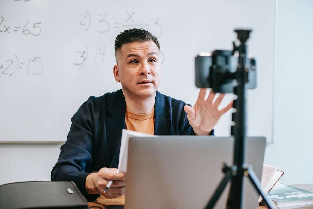 A teacher conducting an online class with a video camera and a laptop in a classroom environment Side Hustles For Teachers