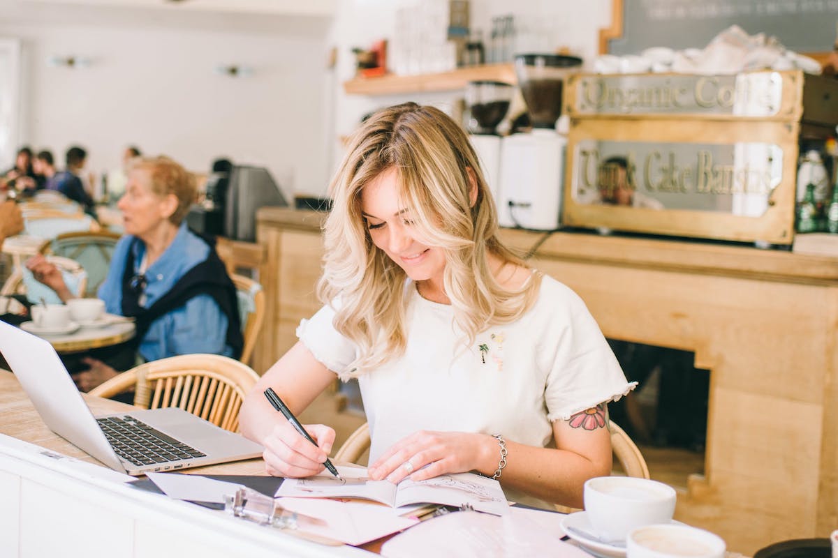 Woman writing in a textbook next to an open laptop. How to Make a Content Marketing Portfolio