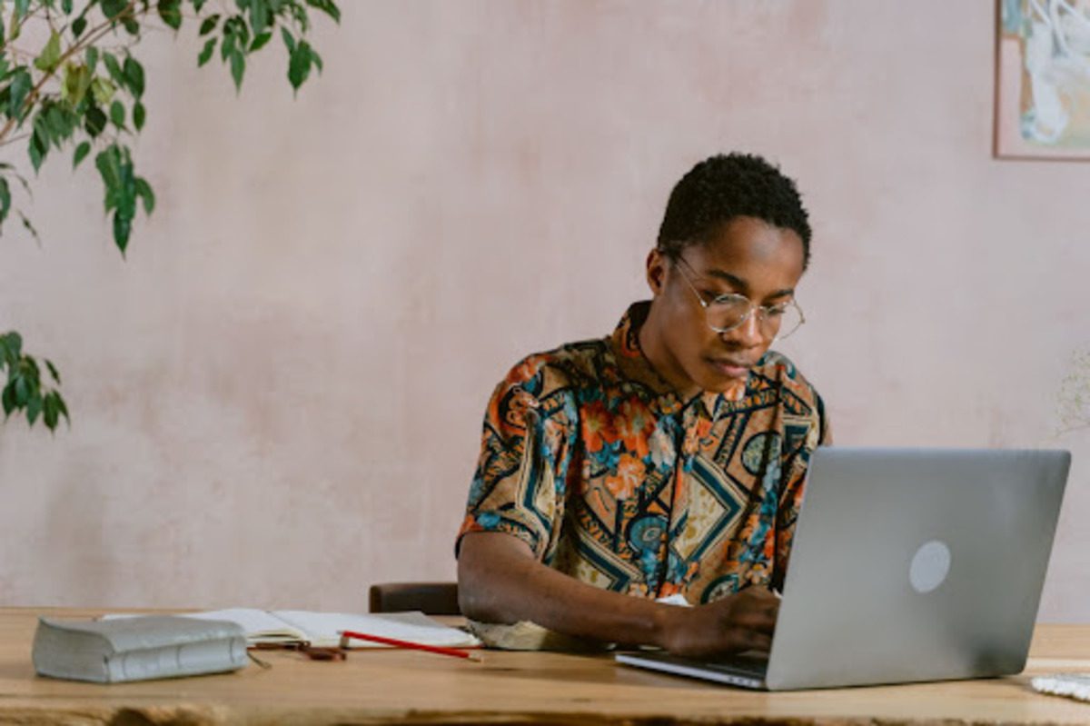 A programmer with glasses and a patterned shirt studying on at a desk with a laptop.