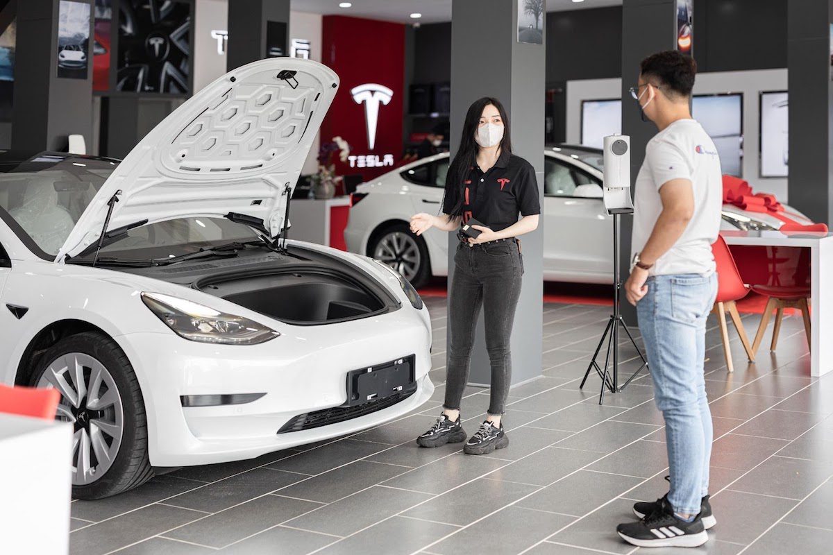 A Tesla employee showcasing an electric car, explaining the specs to a potential customer
