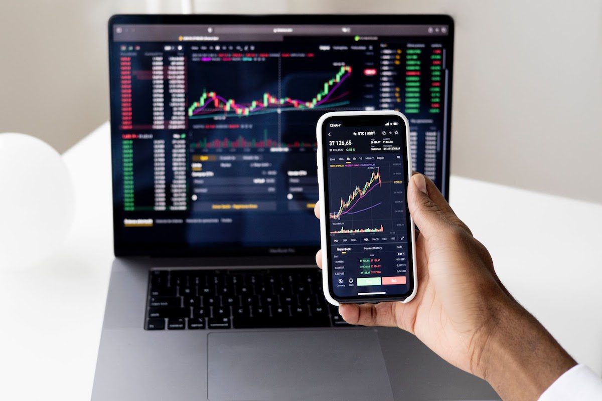 A man checking the stock market on his phone and computer