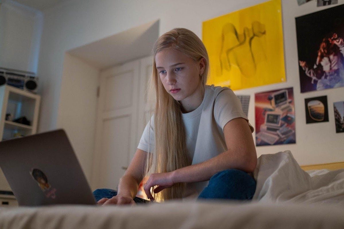 girl sitting on a bed using a laptop