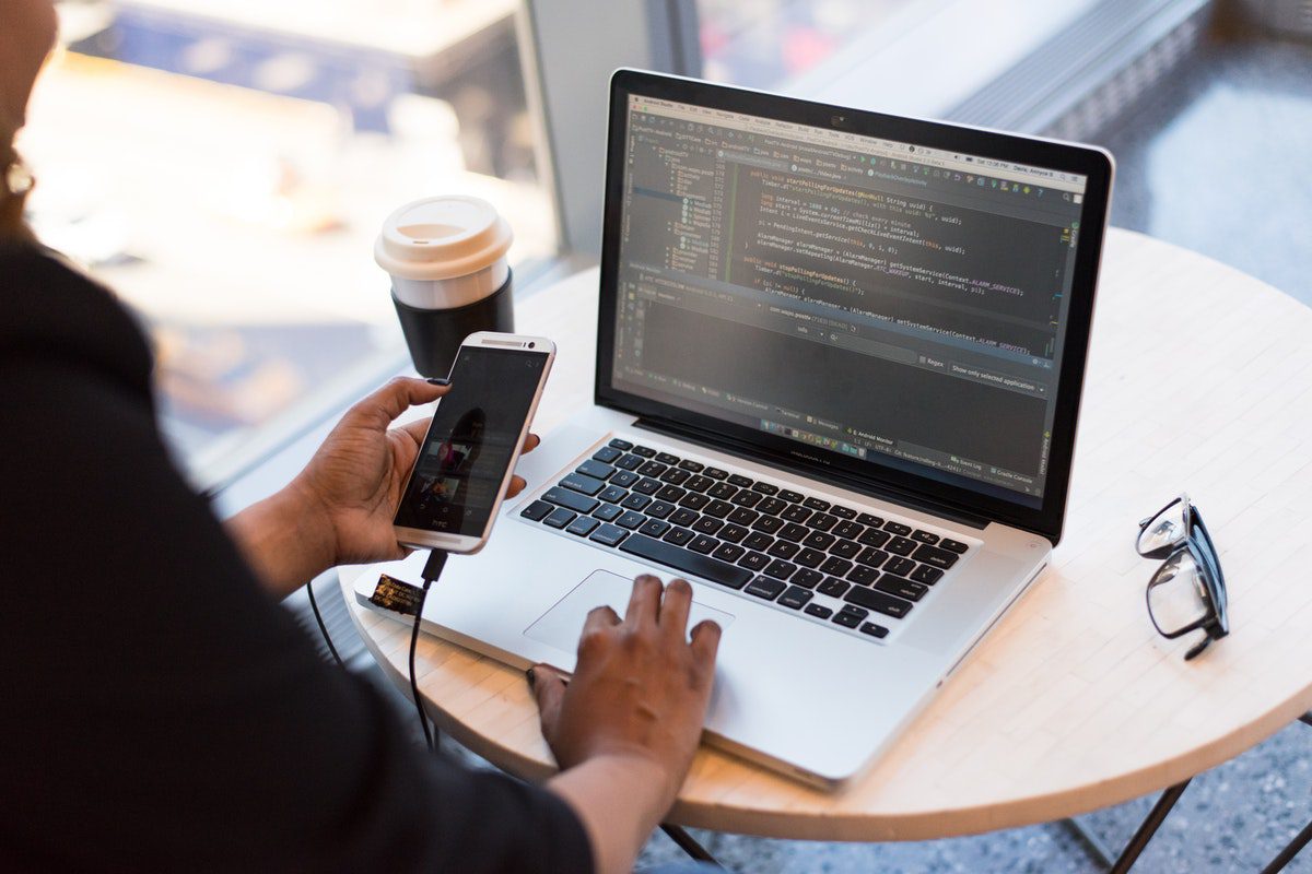 A woman holding a smartphone while using a laptop. Slack Channels for Web Developers