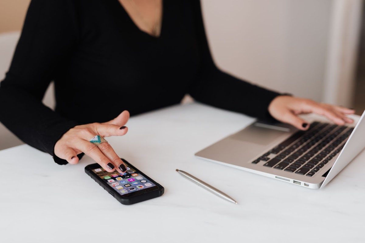 A woman sitting at a desk working on a cell phone and a laptop