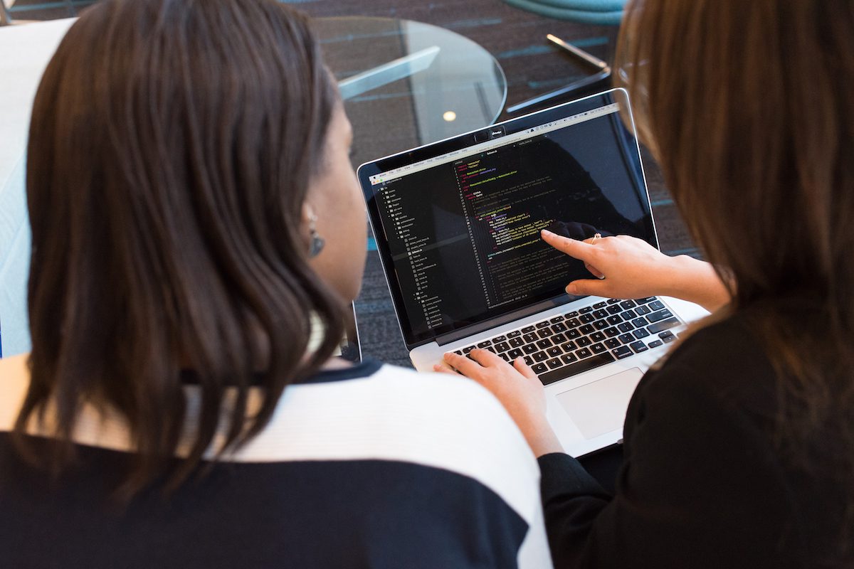 Two women looking at source code in a generic programming language on a laptop.