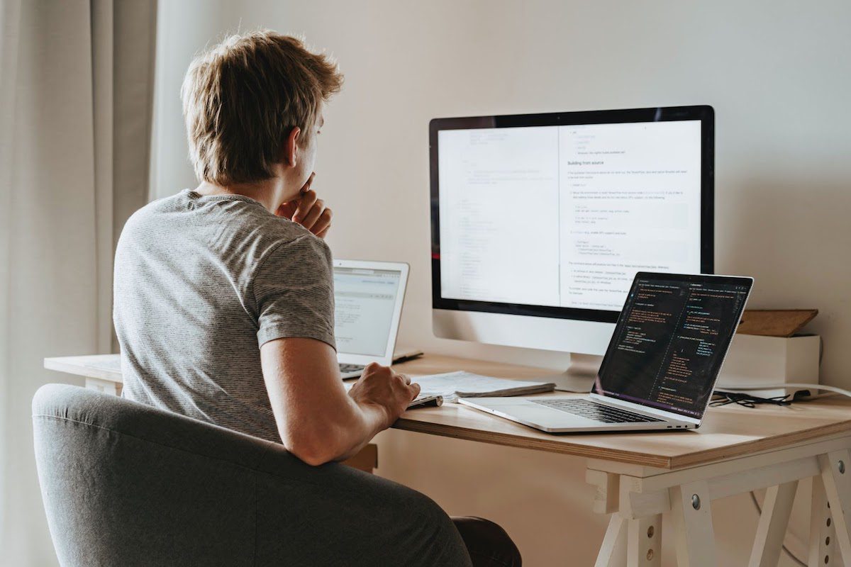 A man sitting at a desk in front of three computers.