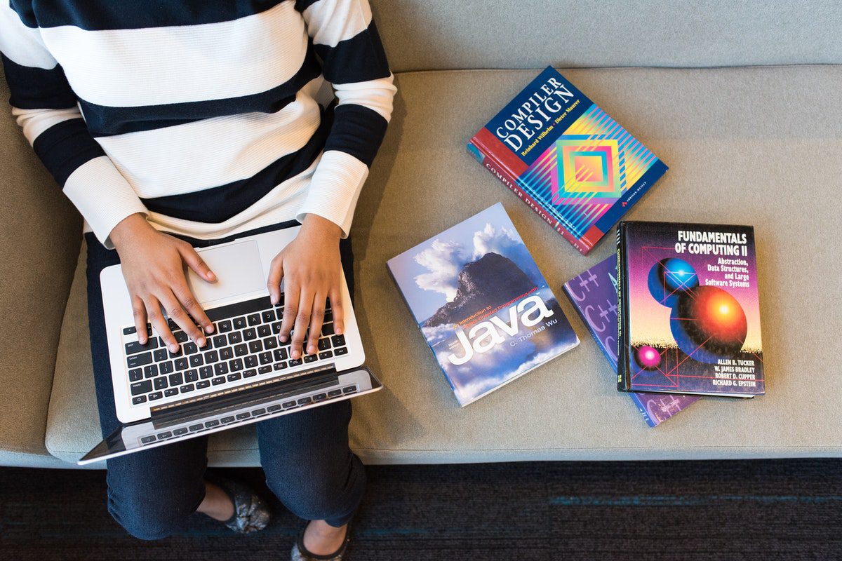 Top-down view of a person using laptop next to programming textbooks. Android Remote Jobs