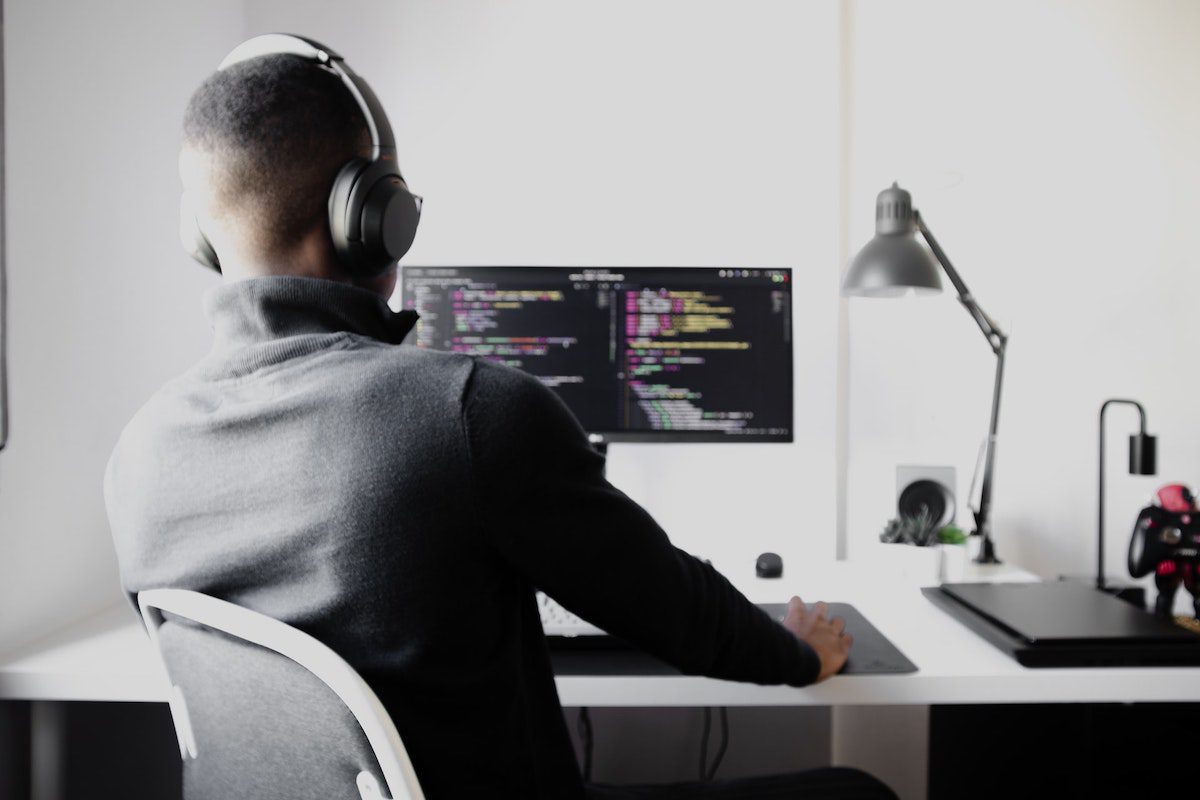A male wearing headphones while sitting at a desk writing lines of code. Python Remote Jobs